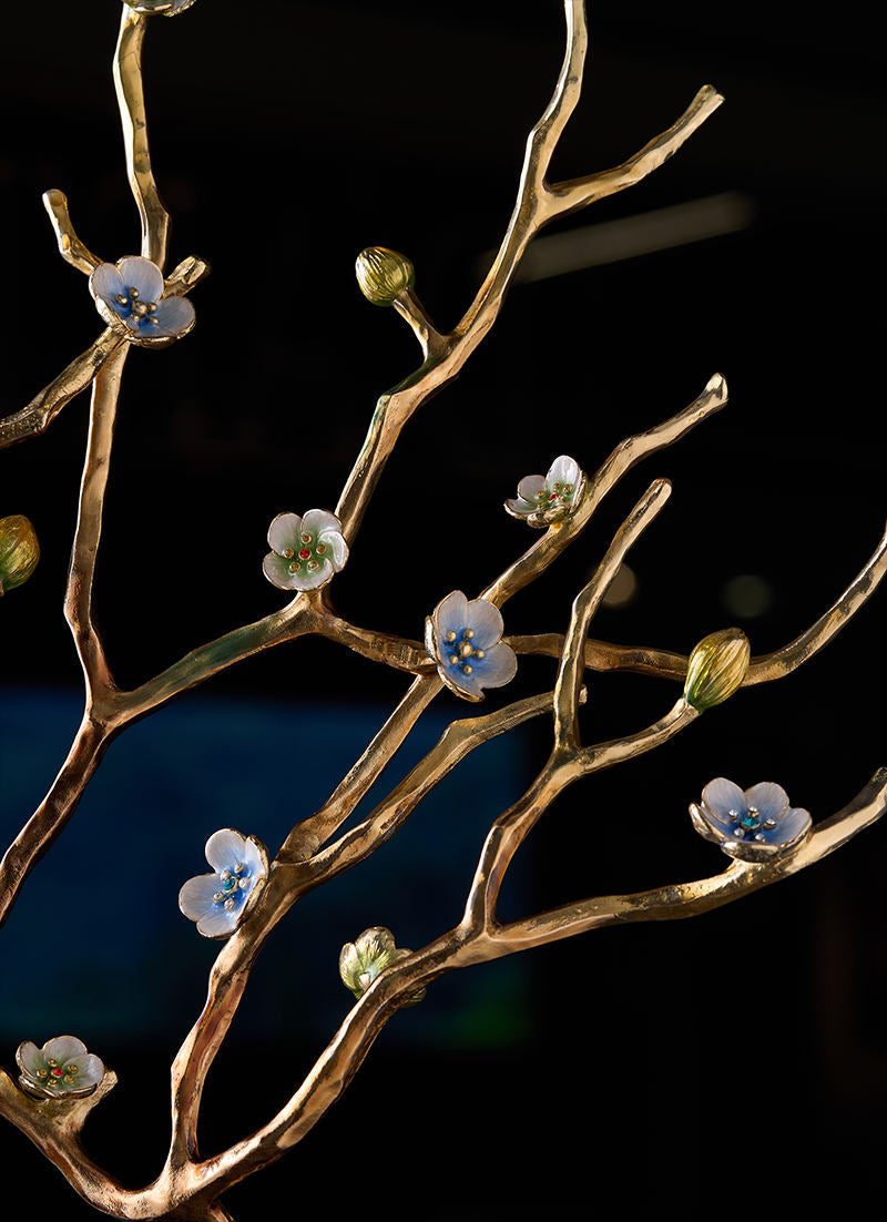 A close-up of a decorative branch sculpture or wall art in textured metallic gold, adorned with small white blossoms and buds with blue and yellow centers, set against a dark background. The brand name SANLOREN is visible in the bottom right corner.